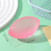 A pink football shaped squishy fidget toy is shown on a green surface next to a white basket.