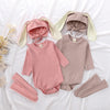 A pink and beige rabbit romper set for babies includes a matching hat and socks laid out on white fabric.