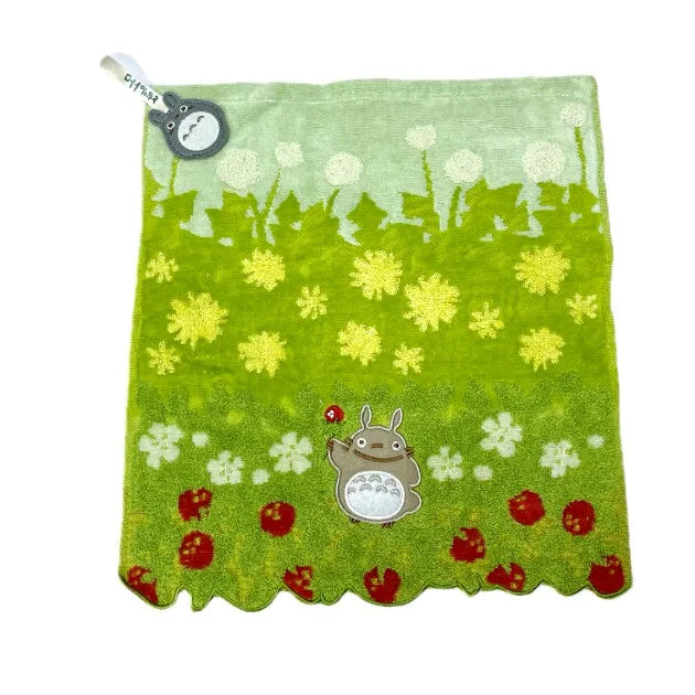 A bright green fabric towel featuring a pattern of white flowers and small yellow plants, with a small gray hippo plush toy a