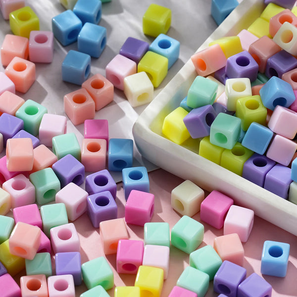 A close-up view of various colorful square acrylic spacer beads scattered on a white surface.