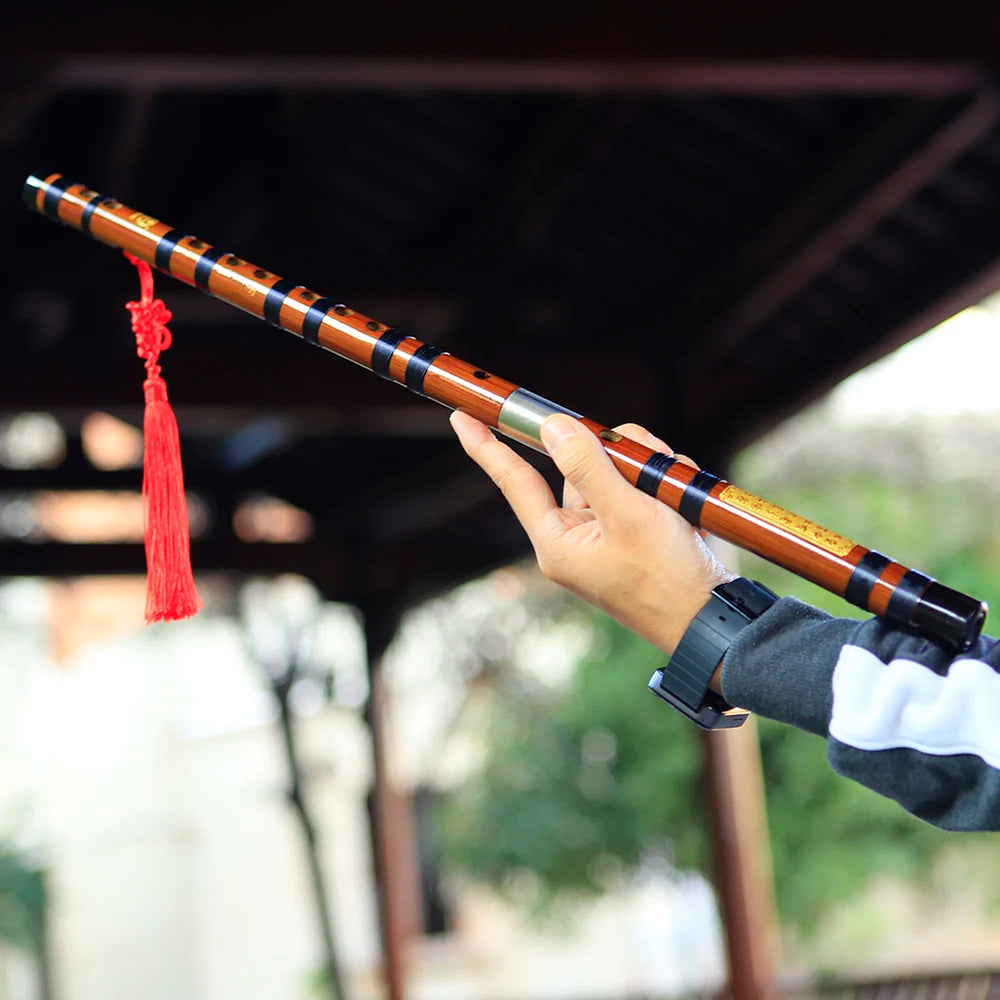 A hand holds a traditional Chinese bamboo flute (dizi) with a brass joint, showcasing the instrument's design.