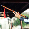 A hand holds a traditional Chinese bamboo flute (dizi) with a brass joint, showcasing the instrument's design.