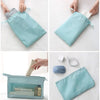 A set of light blue travel packing cubes and a storage bag are shown being handled by hands.