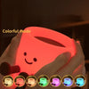 Hands hold a colorful coffee cup shaped night light illuminating a smiling face and various colors.