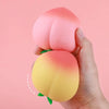 A hand is squeezing a pink, peach-shaped stress relief toy with yellow and orange coloring.