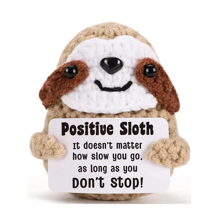 A handmade crochet owl with brown and white feathers smiling and holding a sign that reads Positive Sloth