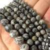 A close-up of natural map jasper loose beads in various shades of gray and black stacked on a hand.