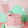 A pink foldable baby potty training seat is displayed on a white stand against a light green background.
