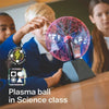 A student in a science class is holding and observing a glowing plasma ball experiment.