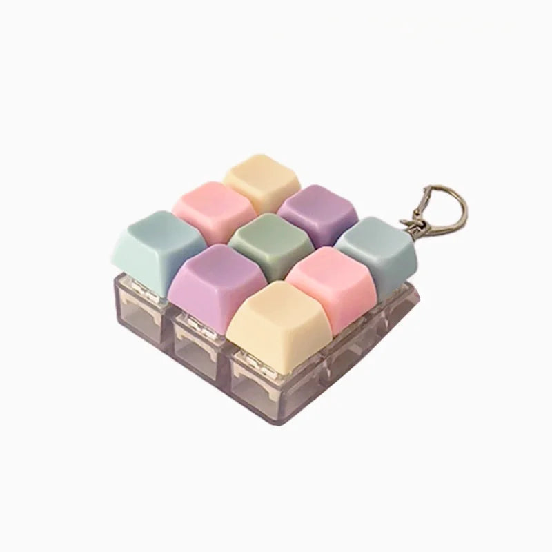A set of colorful silicone clicking keyboard fidget toys in various pastel shades arranged in a tray with a keychain loop.