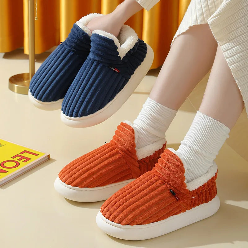A pair of women's cozy faux fur slippers in navy blue and orange are shown on a light surface.