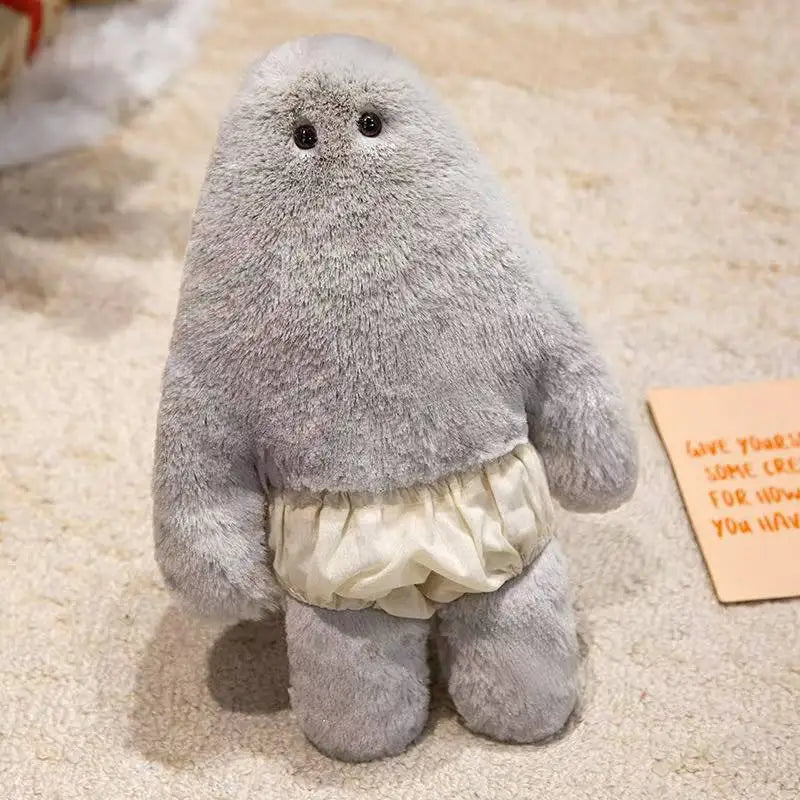 A soft gray monster plush doll with a round body and ruffled pants is shown on a light-colored carpet.
