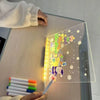 A glowing acrylic message board with seven colorful markers is placed on a light wooden table.