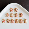A collection of thirty gingerbread resin nail art charms in various shades of brown and red arranged on a white oval dish.