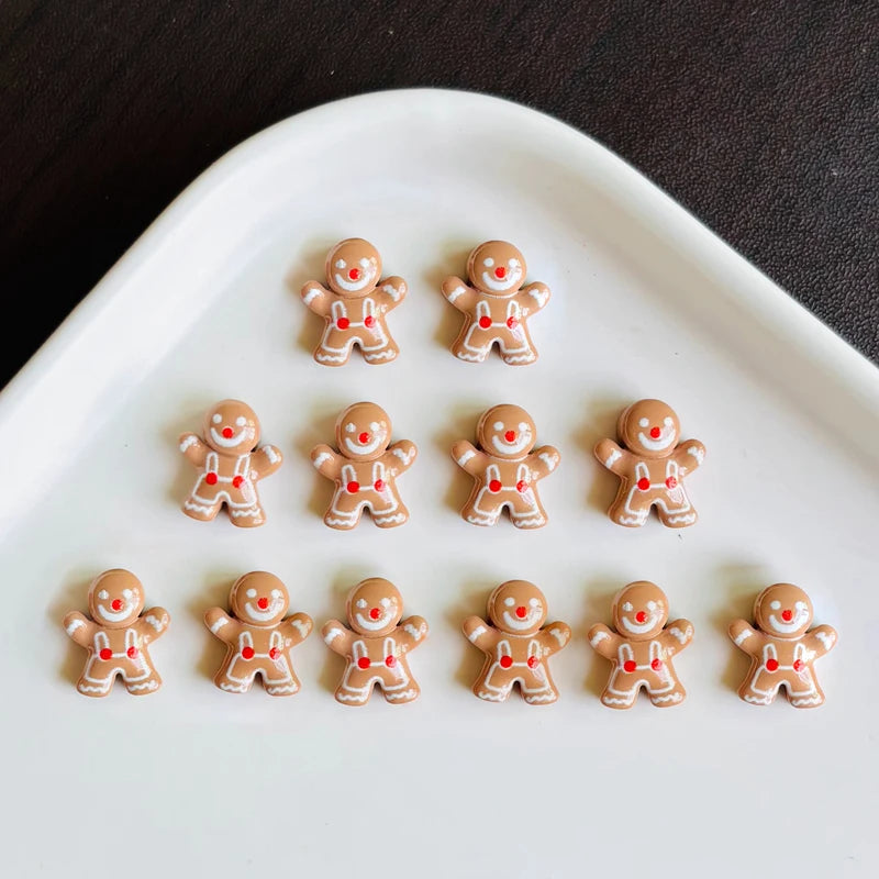 A collection of thirty gingerbread resin nail art charms in various shades of brown and red arranged on a white oval dish.