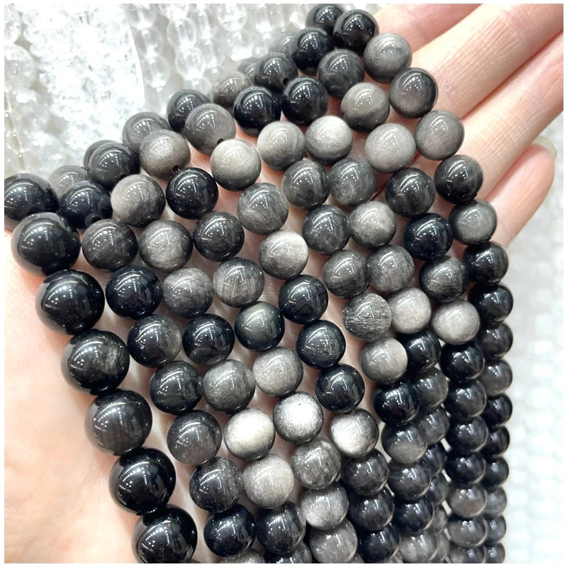 A hand holds a strand of natural stone beads in various shades of black and gray.