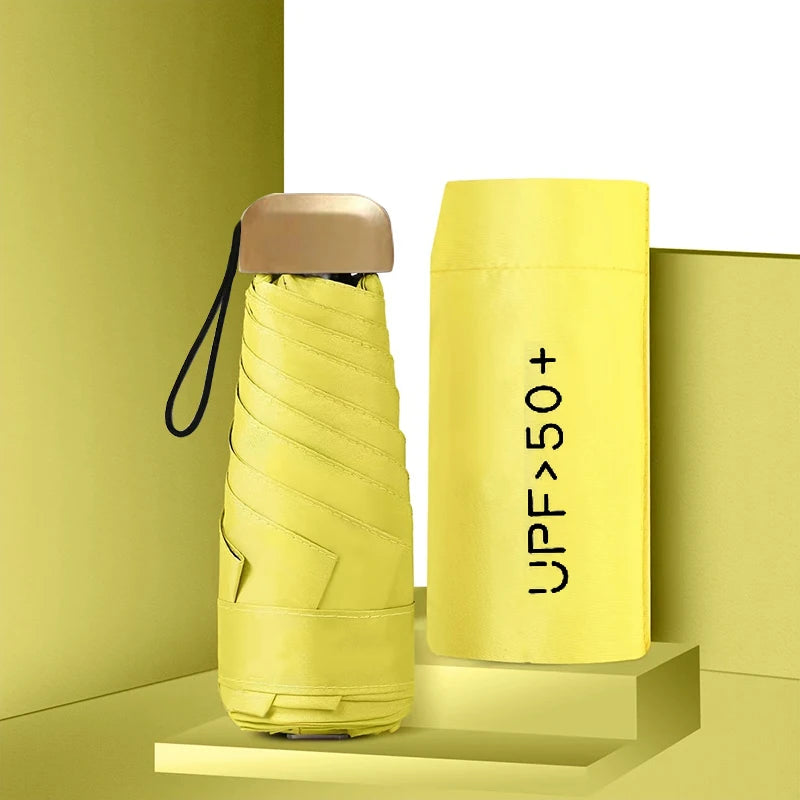 A yellow compact umbrella with a beige handle is displayed against a light green background.