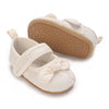 A pair of light beige lace-trimmed baby girl moccasin shoes with a bow, shown from the top and side.