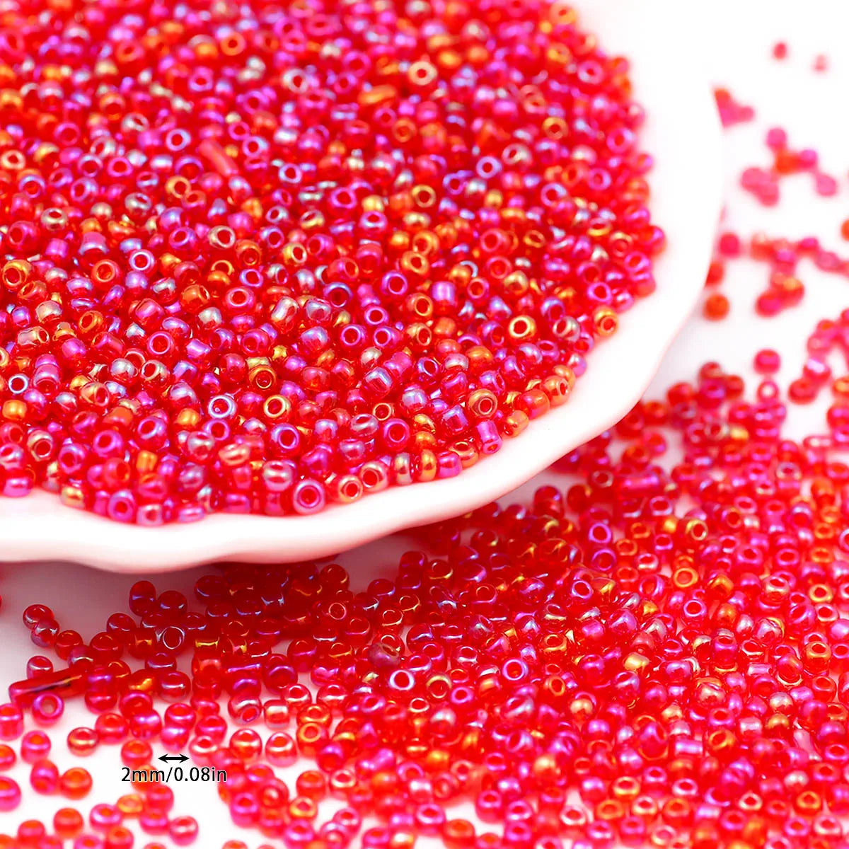 A close-up view of bright red glossy glass seed beads scattered on a white dish and spilled onto a surface.