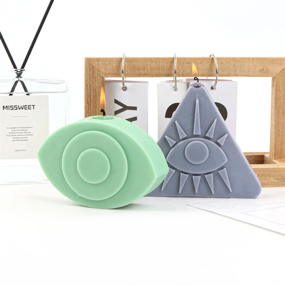 A light green silicone mold shaped like an evil eye is displayed next to a wooden frame and candles.