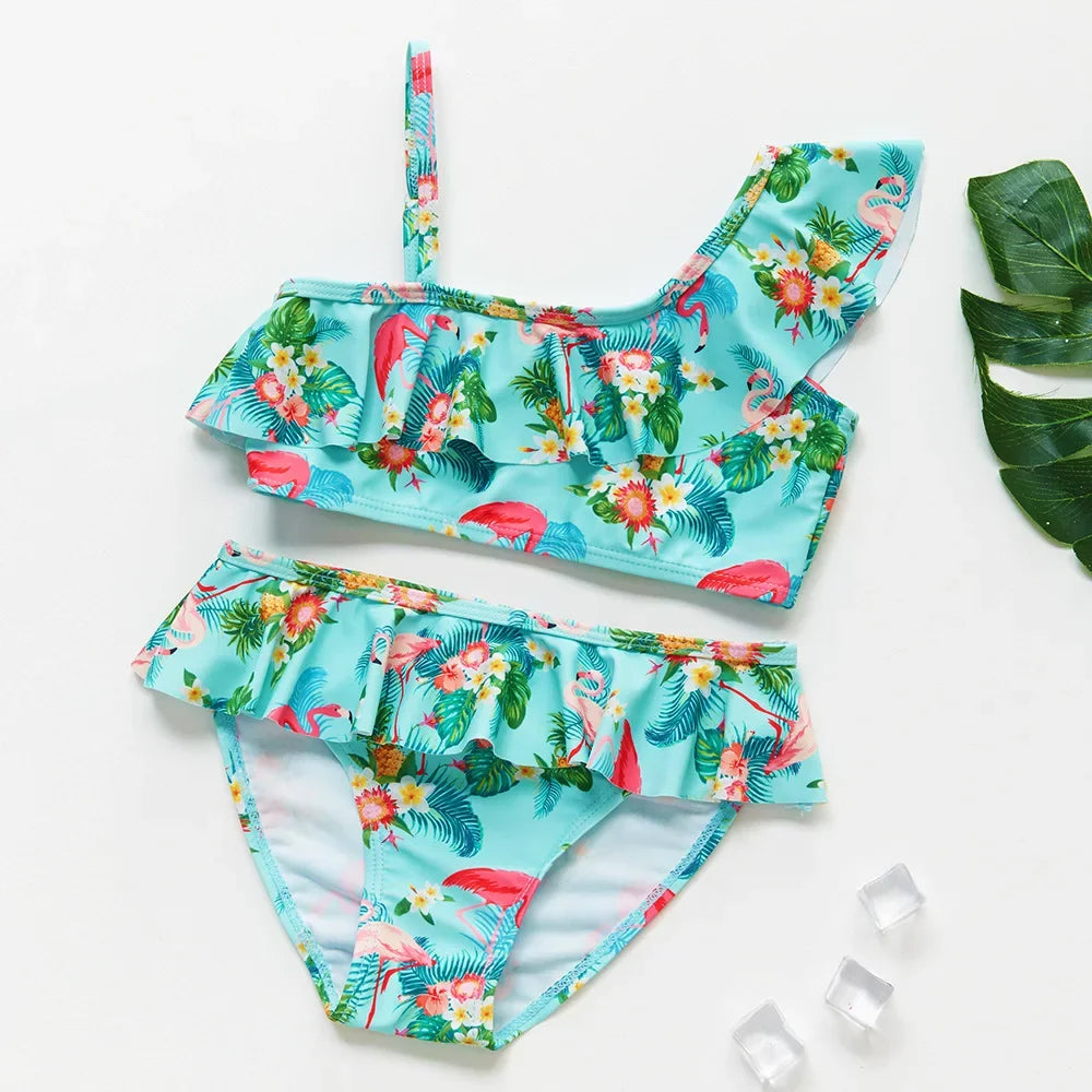 A turquoise and floral two-piece swimsuit set for girls featuring tropical leaves and colorful flowers.