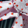 A close-up of a pink long-sleeve shirt for a baby girl with a white background and red strawberry print.