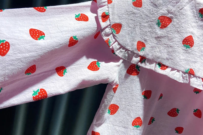 A close-up of a pink long-sleeve shirt for a baby girl with a white background and red strawberry print.