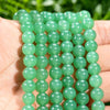 A hand holds a strand of green aventurine gemstone beads for jewelry making.