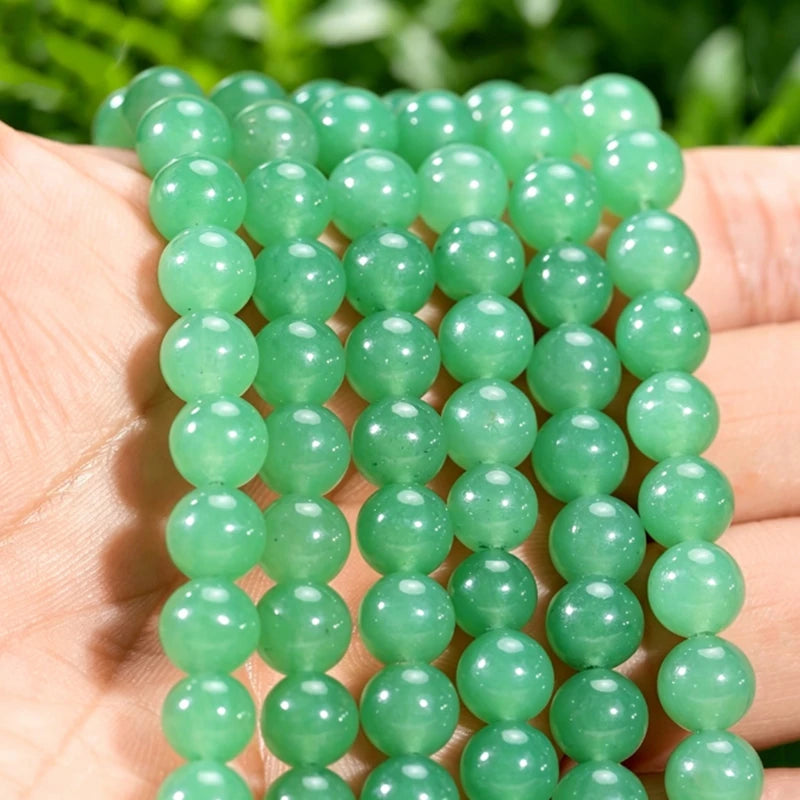 A hand holds a strand of green aventurine gemstone beads for jewelry making.