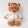 A fluffy brown teddy bear plush toy wearing a white collared shirt and pants with an eye mask and birthday cake decoration.