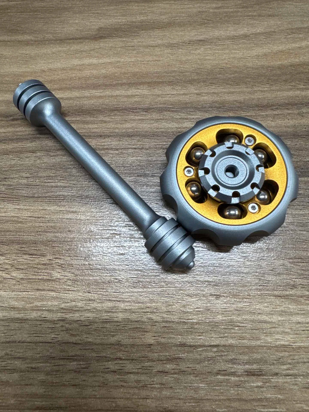 A metal fidget toy featuring a long rod and a circular, textured head with small metal components.