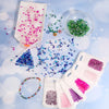 Assortment of faceted crystal glass beads in various colors and shapes scattered on a light blue surface.