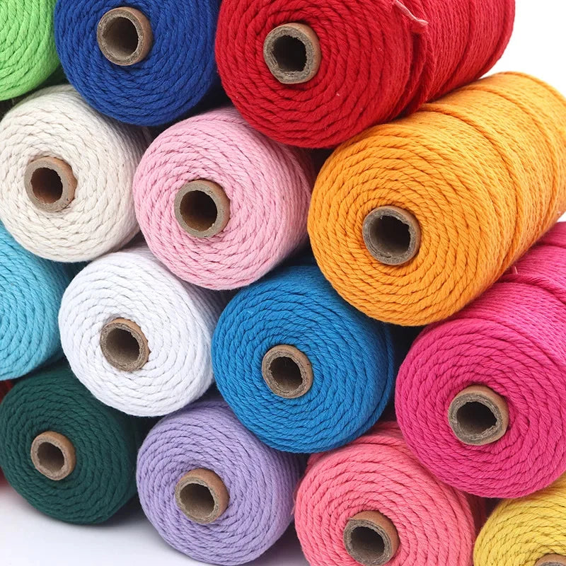 A collection of spools of red, blue, pink, white, and yellow cotton macrame cord for DIY crafts.
