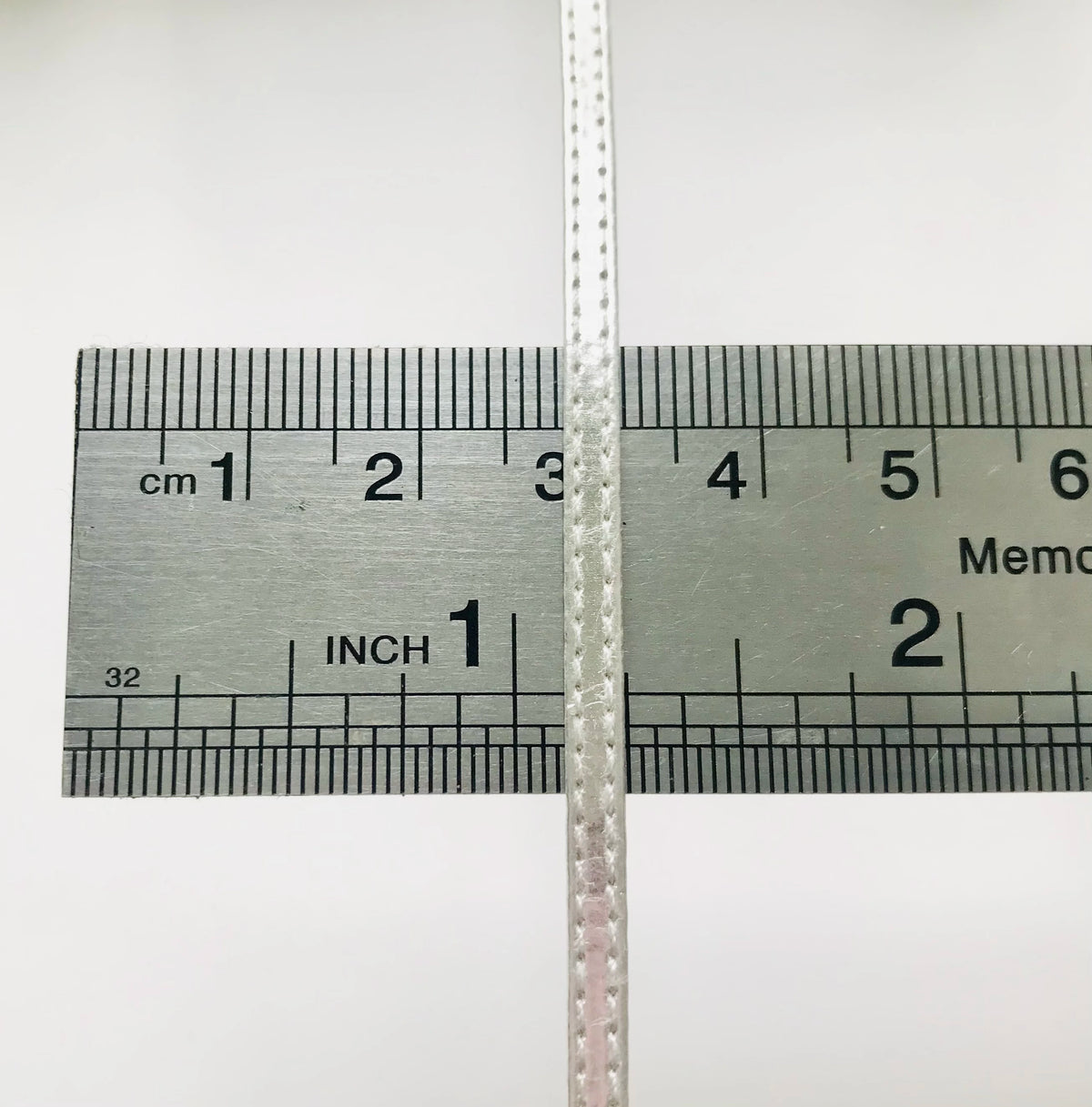 Silberner Lineal mit Zentimetern und Zollmarkierungen, zeigt ein Kreuzsymbol.