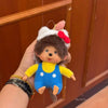 A plush monkey charm pendant featuring a brown face, yellow shirt, and blue overalls with white trim.