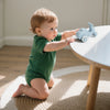 A baby is playing with a light blue silicone toy car on a white table.
