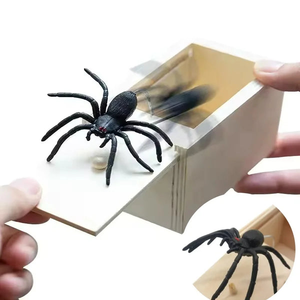 A black spider is visible inside a wooden prank box being held by a hand.