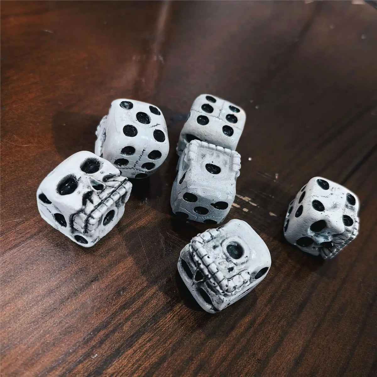 A collection of small white skull dice used for games or Halloween decoration, resting on a dark wooden surface.