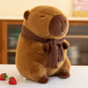 A brown plush capybara stuffed animal wearing a matching knit scarf, sitting on a white surface next to a strawberry.