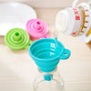A clear glass bottle is being filled with oil using a white funnel, next to colorful silicone funnels.