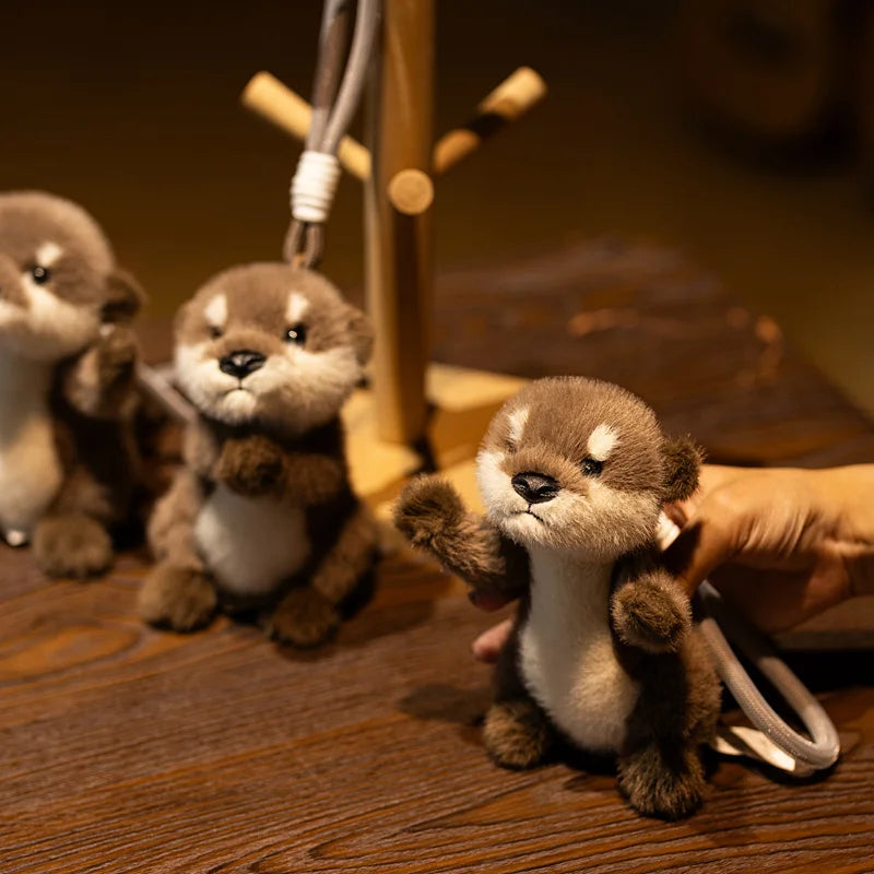 A small brown and white plush otter is displayed on a wooden surface, attached to a keychain.