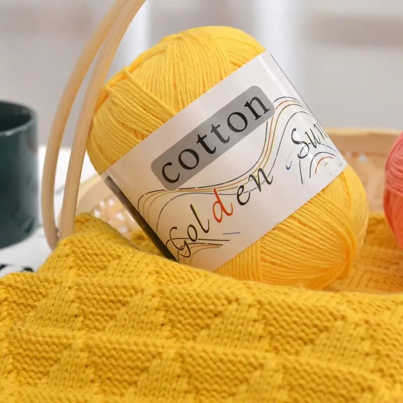 A ball of bright yellow cotton knitting yarn labeled Golden Swirl resting on a yellow knitted fabric.
