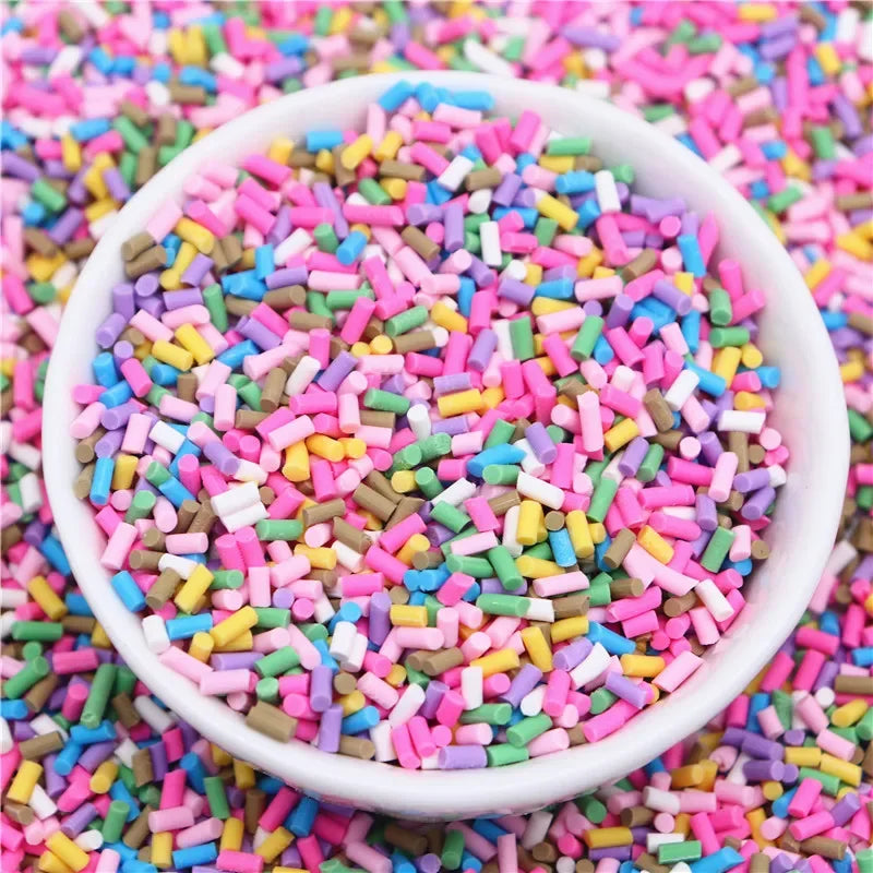 A white bowl filled with colorful polymer clay slice sprinkles for slime and DIY crafts scattered on a pink surface.
