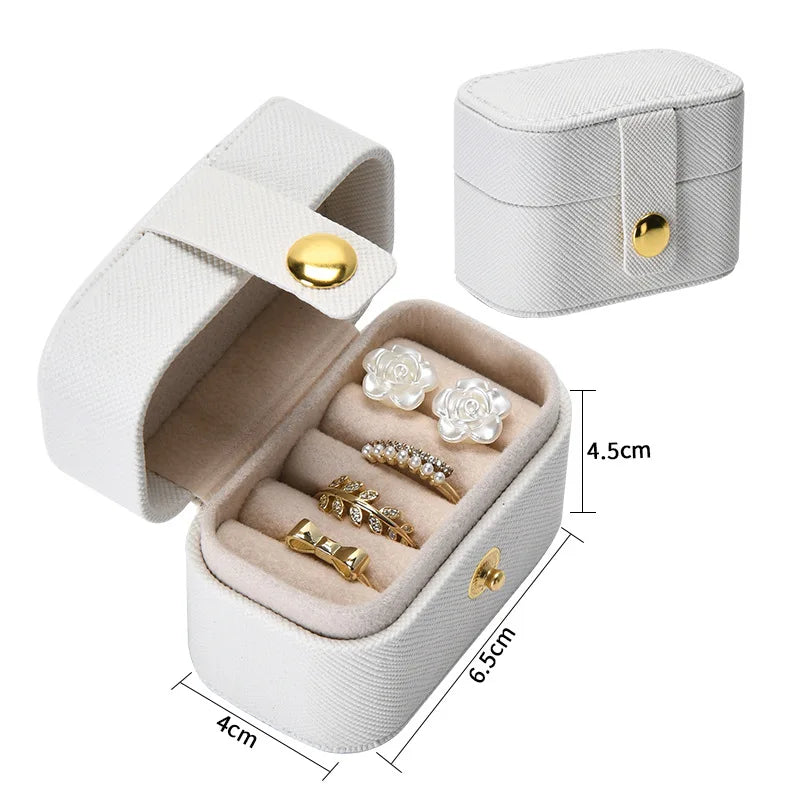 A white portable leather jewelry storage box with a lid open, displaying several pieces of gold and silver jewelry.