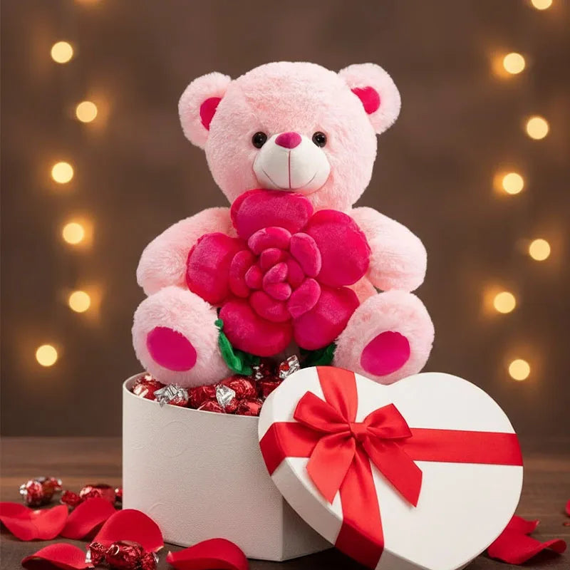 A pink plush bear holding a large pink rose, presented in a white box with red ribbon and surrounded by red petals.