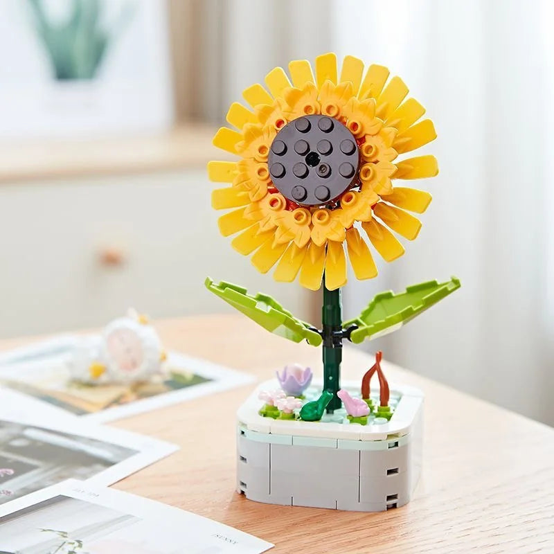 A yellow sunflower building block bouquet set with green stems and pink flowers on a wooden table.