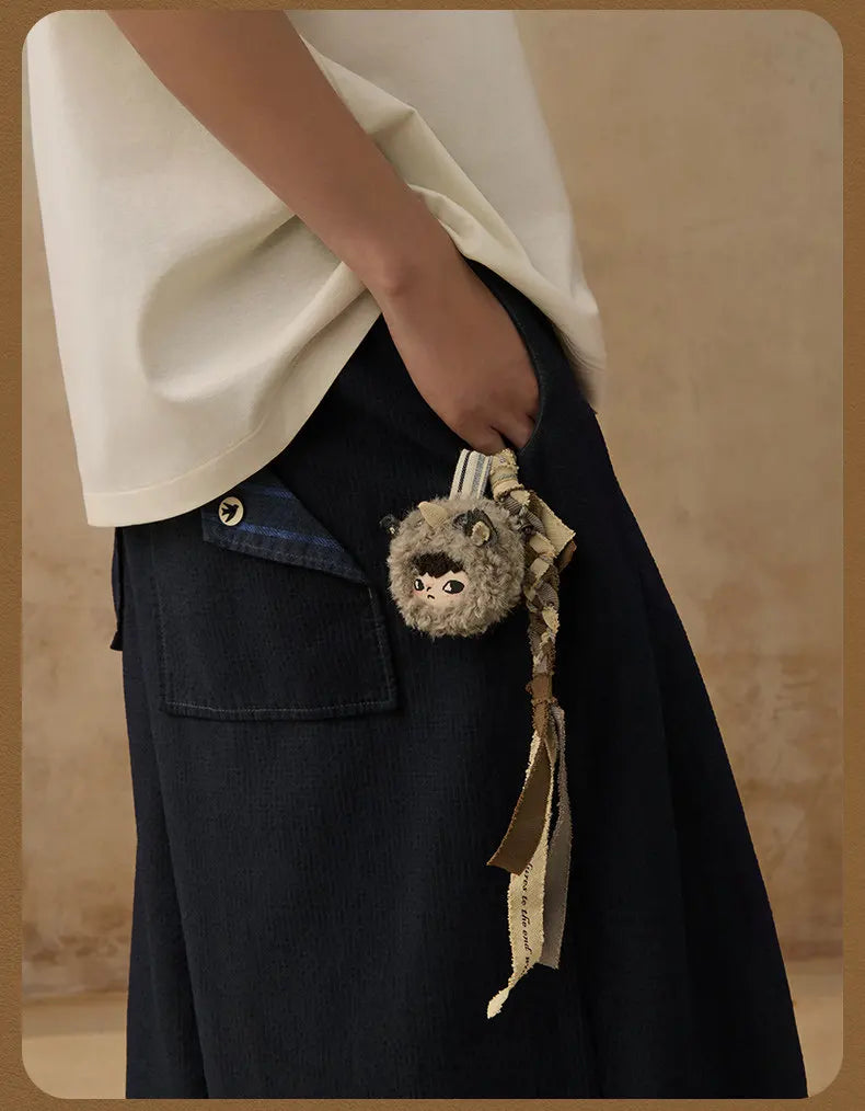 A dark navy fabric garment with a pocket features a small keychain charm of a gray animal.