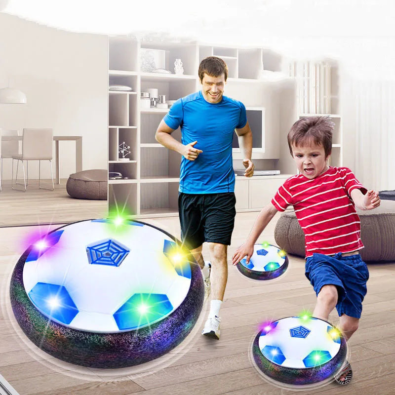 A boy is kicking a glowing LED hover soccer ball in a bright room.