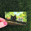A card featuring cute black and white cats sitting on a wooden ledge against a bright green background.