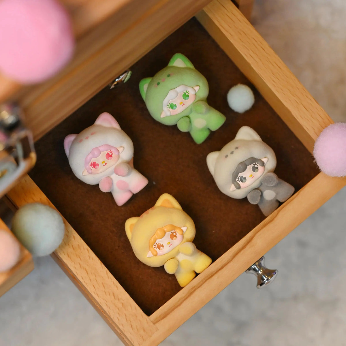 A wooden box contains several small, cute cat-shaped figurines in various pastel colors like green, pink, and yellow.